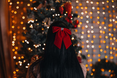 A brunette woman with a red bow in her hair sitting near the christmas tree with festive decorations
