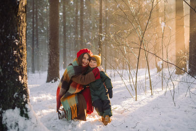 Portrait of young attractive mother in warm clothes and her little son in beautiful snowy forest.