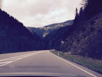 Empty road by mountains against cloudy sky