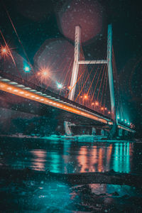 Illuminated suspension bridge over river against sky at night