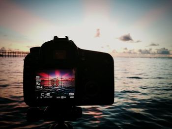 Close-up of camera against sea and sky during sunset