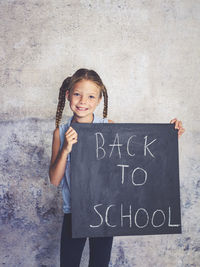 Portrait of smiling girl holding writing slate with text against wall