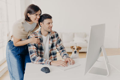 Smiling couple using computer by dog on sofa at home
