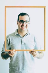 Portrait of young man holding empty picture frame against white background