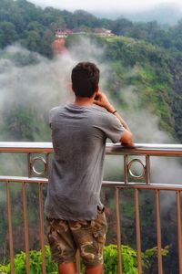 Rear view of boy standing against railing 