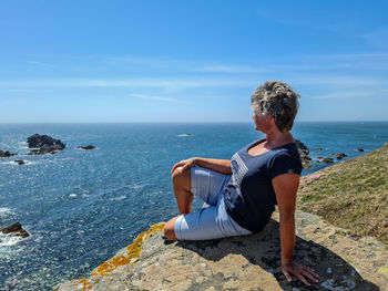 Woman sitting on rock looking at sea against sky