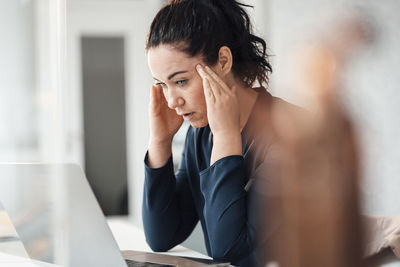 Stressed businesswoman with head in hands looking at laptop on table