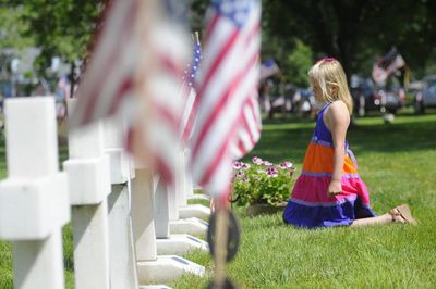 Side view of girl kneeling by tombstones in cemetery