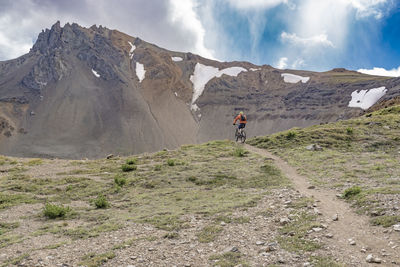 Rear view of man climbing on mountain against cloudy sky