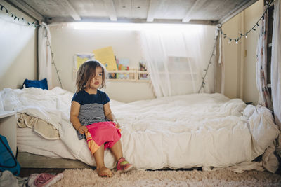 Girl wearing clothes while sitting on bed at home