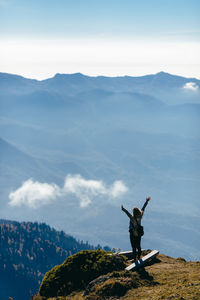 Man with arms raised on mountain against sky