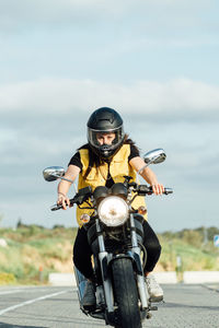 Focused female bike in helmet riding modern motorbike along road on sunny day and looking at camera