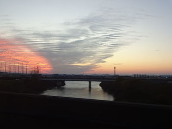 Silhouette bridge over river against sky during sunset