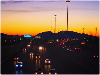 Cars on illuminated road against dramatic sky during sunset