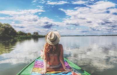 Rear view of woman sitting in lake against sky