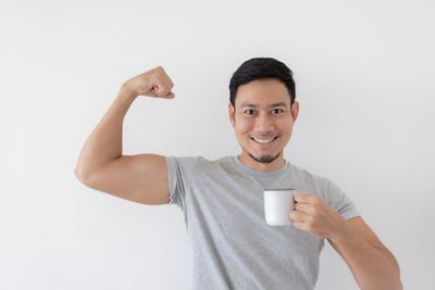 Portrait of young woman with arms raised standing against white background