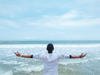 Rear view of a man with arms raised against sea