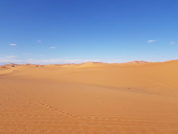 A desert landscape with a blue sky and footprints in the sand