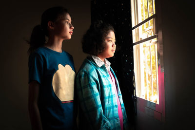 Two young girls best friends stood looking at the window of a house with lonely faces.