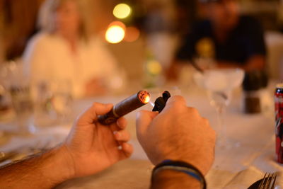 Cropped hands of man lighting cigar on table