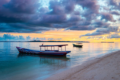 Boat moored on sea against sky during sunset