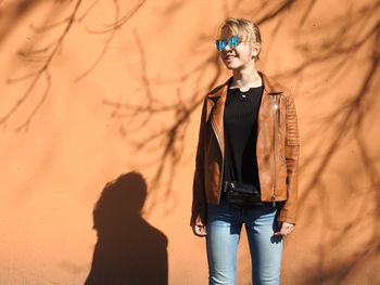 Smiling woman wearing sunglasses while standing against wall