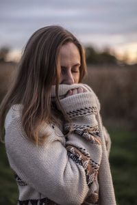 Young woman with eyes closed standing on field against sky during sunset