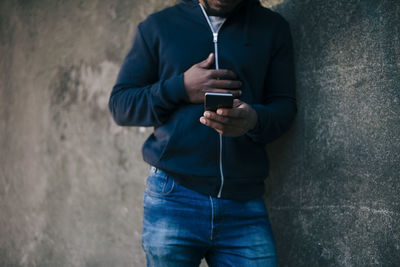 Midsection of young man leaning on wall while using smart phone