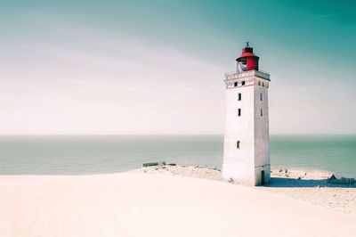 Lighthouse on beach by sea against sky