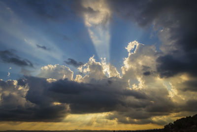 Low angle view of sunlight streaming through clouds