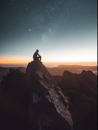 Silhouette man standing on rock against sky at night