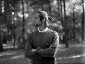 Young man with arms crossed looking away while standing in forest