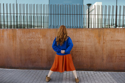 Rear view of woman standing with legs apart while facing wall