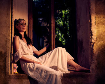 Portrait of woman sitting on window at night