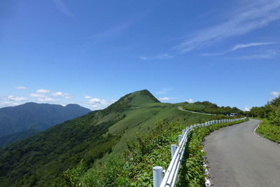Scenic view of road leading towards mountains against blue sky