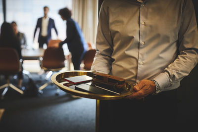 Midsection of professional holding mobile phones in tray at board room