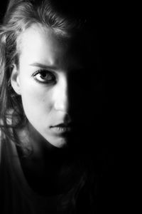 Close-up portrait of serious beautiful woman against black background