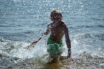 Rear view of boy splashing water in sea