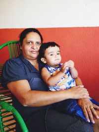 Portrait of grandmother with grandson sitting on chair against wall