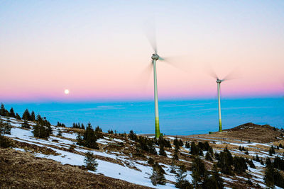 Wind turbines on land against sky during sunset