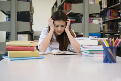 Tensed female student studying at table in library