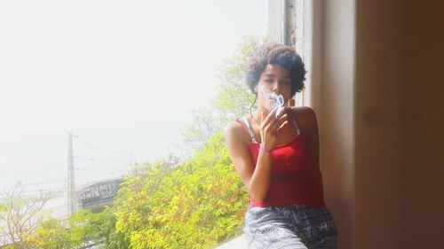 Young woman smoking while sitting at window sill