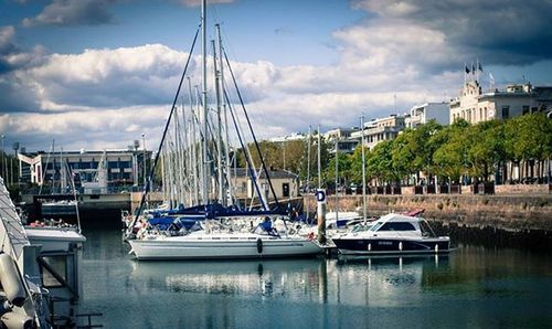 Sailboats moored at harbor against cloudy sky