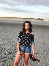 Portrait of teenage girl standing at beach against sky