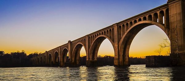 Arch bridge over river against sky during sunset