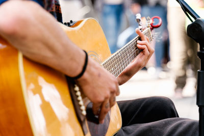Selective focus on the hands of a young man playing a guitar in a crowded street