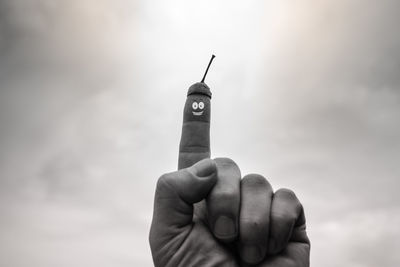 Close-up of hand holding cross against sky