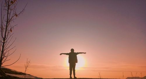 Silhouette man with arms outstretched standing against sky during sunset