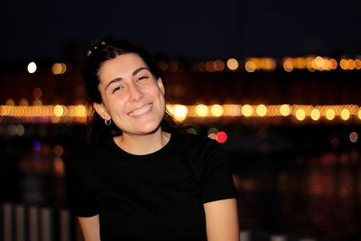 Portrait of young woman standing against illuminated lights at night