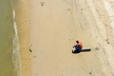 High angle view of shirtless man sitting at beach during sunny day